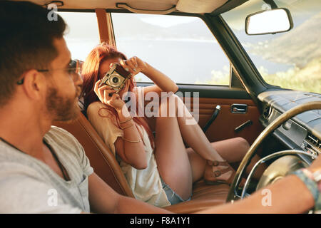 Coppia caucasica andando su un viaggio su strada. Donna di scattare foto con la fotocamera e uomo alla guida di auto.
