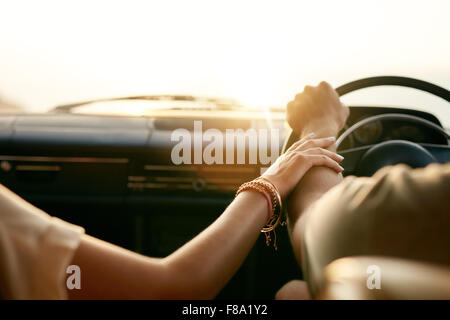 Vista posteriore di una giovane coppia tenendo le mani mentre è seduto nella loro auto insieme. L uomo e la donna in un viaggio su strada. Foto Stock