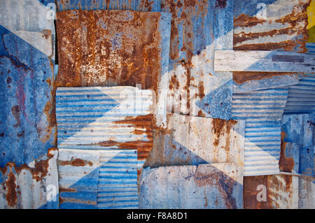 Un abstract immagine di sfondo della bandiera della Scozia dipinta su di rusty ferro corrugato fogli sovrapposti per formare una parete Foto Stock