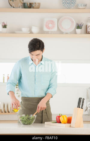 Uomo che indossa un grembiule e facendo una insalatiera in cucina Foto Stock