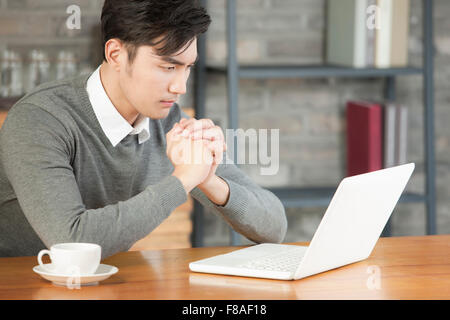 Uomo con le mani incrociate seduti al tavolo e guardando il computer portatile Foto Stock