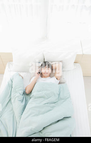 Elevato angolo di un uomo disteso nel letto a parlare al telefono Foto Stock