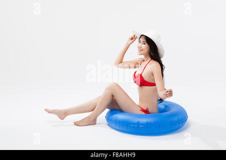 Donna asiatica in rosso per la zona bikini e indossare un cappello bianco seduto su un tubo blu Foto Stock