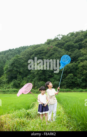 Un ragazzo e una ragazza in piedi con le reti sulla corsia attraverso i campi di riso in primavera Foto Stock