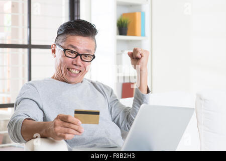 Ritratto di 50s coppia uomo asiatico premi mentre si utilizza il computer internet facendo di pagamento online con carta di credito, seduti su Foto Stock