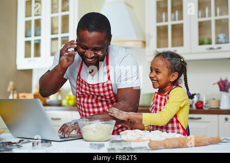 Giovane uomo chiamando e networking in cucina con sua figlia nelle vicinanze Foto Stock