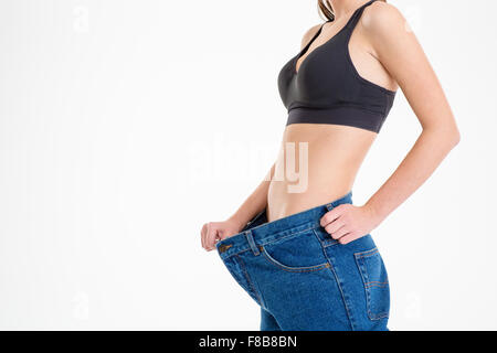 Giovani sportive con bel corpo in vecchi jeans grandi che mostra quanto peso ha perso su sfondo bianco Foto Stock