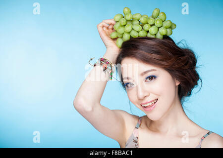 Donna sorridente e mettendo le uve sulla sua testa Foto Stock