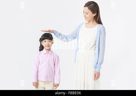 Madre e figlia in piedi accanto a ogni altra madre e figlia di misurazione dell'altezza ponendo la sua mano sopra la figlia della testa Foto Stock