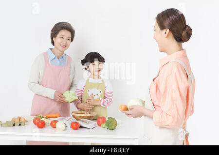 Madre tenendo una piastra con verdure e guardando la figlia e la nonna cucinare insieme Foto Stock