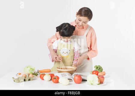 Madre e figlia cucina insieme con una varietà di verdure e altri ingredienti alimentari messi sul tavolo Foto Stock