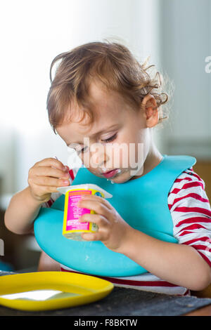 2 anno-vecchio ragazzo di mangiare uno yogurt. Foto Stock