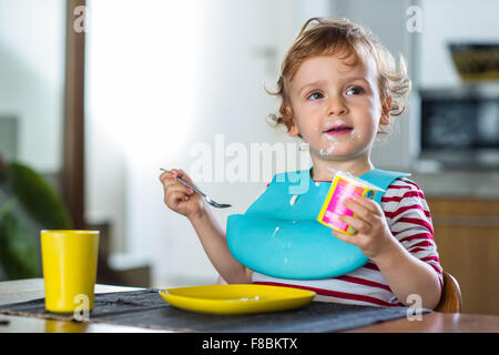 2 anno-vecchio ragazzo di mangiare uno yogurt. Foto Stock