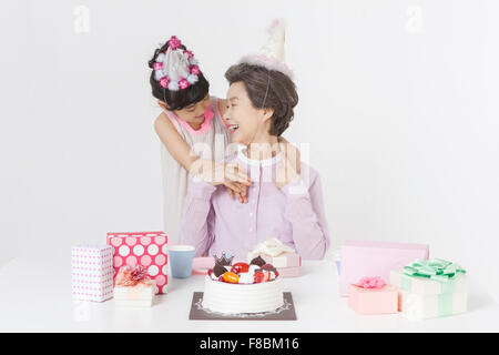 Nonna e nipote in party cappelli festeggia il compleanno sia guardando ogni altro e una torta con confezioni regalo posto Foto Stock