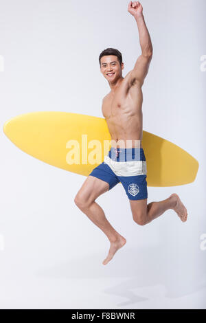 Uomo muscolare tenendo un surf board sotto il suo braccio e salto con la sua mano alta Foto Stock