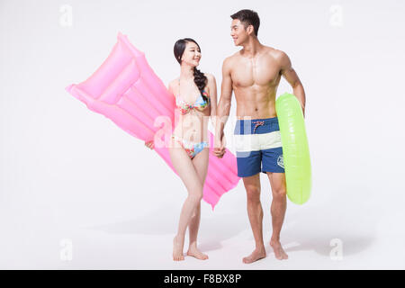 Donna in bikini azienda un galleggiante sotto il suo braccio e un uomo in pantaloni di nuoto tenendo un tubo ad anello sia guardando ogni altro e Foto Stock