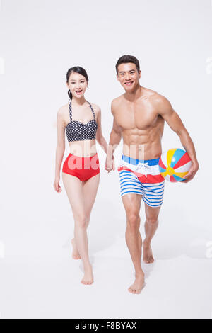 Matura in costume da bagno tenendo le mani insieme e a piedi con una spiaggia palla in mano d'uomo Foto Stock