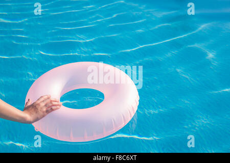 Mano sul gonfiabile rosa tubo tondo galleggianti in piscina Foto Stock