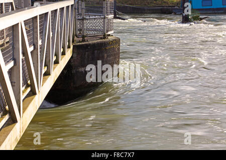 Fast correndo acqua coursing intorno al pilastro di uno stramazzo che mostra solo quanto è veloce che scorre nel fiume gonfio. Foto Stock