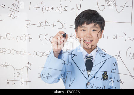Scuola elementare ragazzo di età in uniformi di scuola mostrata dietro un pannello trasparente con formula matematica scritta e la scrittura Foto Stock
