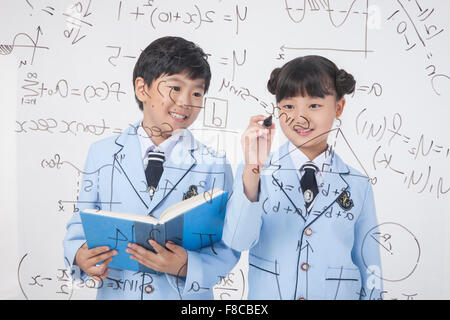 Scuola elementare età un ragazzo e una ragazza in uniformi di scuola mostrata dietro un pannello trasparente con formula matematica e scritte Foto Stock