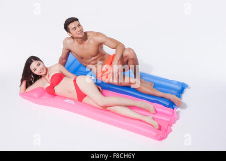 Matura in spiaggia indossare giacente sul loro lato su un galleggiante ogni e sorridente Foto Stock