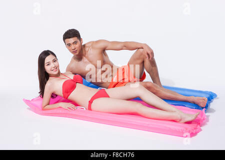 Woman in Red bikini giacente su un galleggiante e un uomo in pantaloni di nuoto che giace accanto a lei con un ginocchio sollevato sia con lo sguardo in avanti Foto Stock