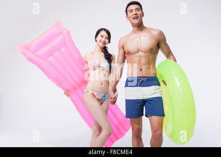 Donna in bikini tenendo un galleggiante e un uomo in pantaloni di nuoto tenendo un tubo ad anello con mano nella mano insieme sia guardando verso l'alto Foto Stock