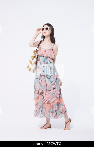 Donna con capelli lunghi in abito maxi in piedi con la sua borsa sulla sua spalla e guardando in alto Foto Stock