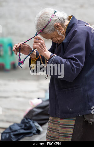 Vecchia e povera donna tibetano durante la sua cerimonia religiosa Foto Stock