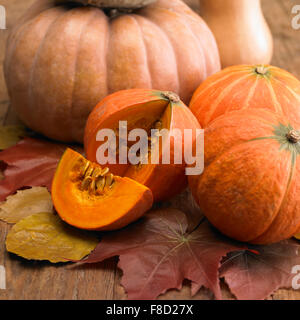 Zucche e una fetta di zucca che mostra il suo interno sulla caduta foglie Foto Stock