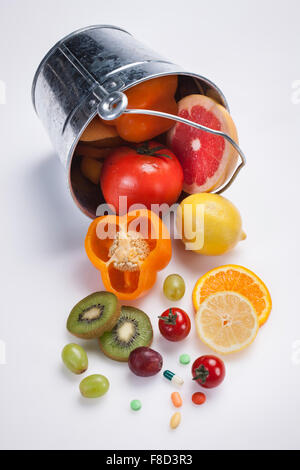 Elevato angolo di freschi fette di frutta e verdura con vitamina pillole rovesciato da un bucket Foto Stock