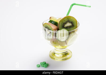 Il colore verde la frutta e la verdura fette in un bicchiere con una cannuccia e un colore verde integratori nutrizionali pillole accanto ad esso Foto Stock