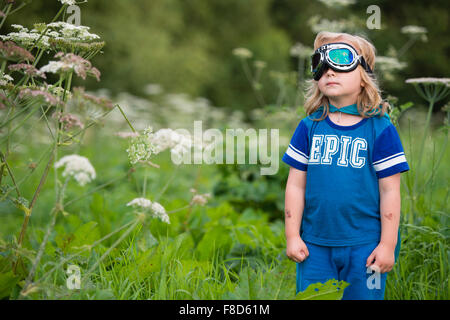 Un piccolo pre-teen boy in una casa fatta di costume e occhiali vestito e giocare all'aperto presso essendo Mini supereroe in una serata estiva , REGNO UNITO Foto Stock