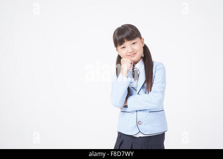 Scuola elementare età ragazza con i capelli in mazzetti in uniformi di scuola con lo sguardo in avanti con un sorriso con la sua mano sulla mento Foto Stock