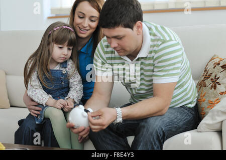 Giovani parrent a casa con bel bambino realizzare risparmi e messo monete soldi nel salvadanaio Foto Stock