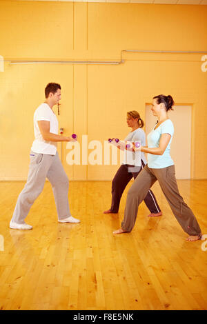 Due donne facendo esercizi con manubri con personal trainer in palestra Foto Stock