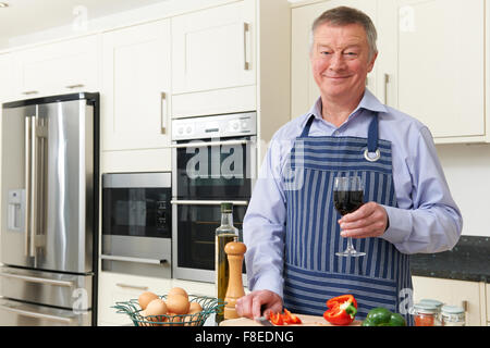 Senior uomo godendo la cottura in cucina con bicchiere di vino Foto Stock
