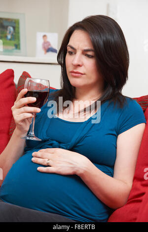 In questione donna incinta di bere un bicchiere di vino in casa Foto Stock