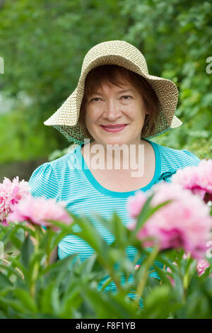 Donna matura in peonia pianta in giardino Foto Stock