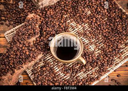 Tazza di caffè e caffè in grani sparsi sul vassoio di vimini Foto Stock