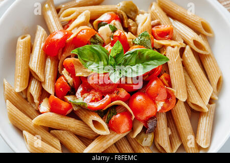 Pasta con i pomodori ciliegia sulla piastra bianca circondata da ingredienti e poggiante su legno scuro tabella Foto Stock