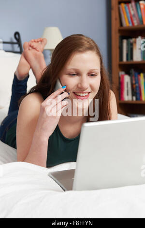 Ragazza adolescente utilizzando notebook e cellulare In camera da letto Foto Stock