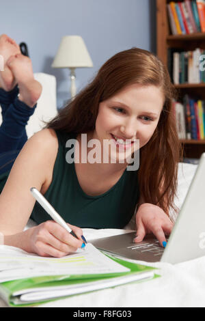 Ragazza adolescente utilizzando laptop per fare i compiti in camera da letto Foto Stock