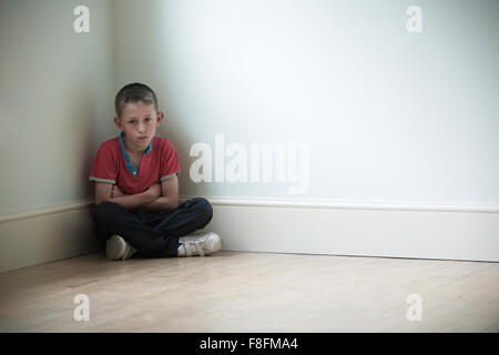 Infelice bambino seduto in un angolo della stanza Foto Stock