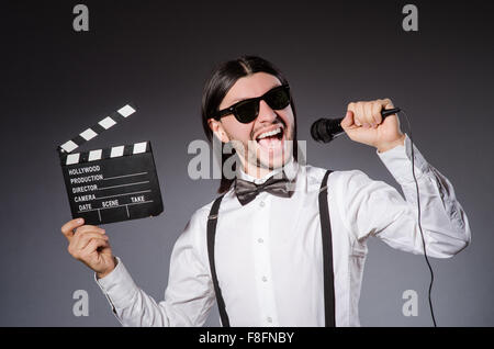 Uomo positivo tenendo clapperboard microfono e isolato su grigio Foto Stock