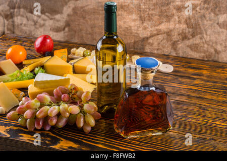 Bottiglia di vino bianco e ambra Whiskey alcol su tavola in legno rustico con varietà di formaggio Gourmet e Uva - Ingredienti per il formaggio del bordo. Foto Stock