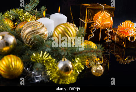 Colorate a tema oro Natale ancora in vita con baubles nestling nei rami di pino a fianco di due eleganti doni in lamina d'oro con archi, sfondo scuro con copyspace. Foto Stock