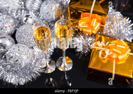Natale di lusso ancora in vita con due flauti di champagne, decorato oro regali e una disposizione di tinsel argento e decorazioni di Natale visto elevato angolo su uno sfondo nero. Foto Stock