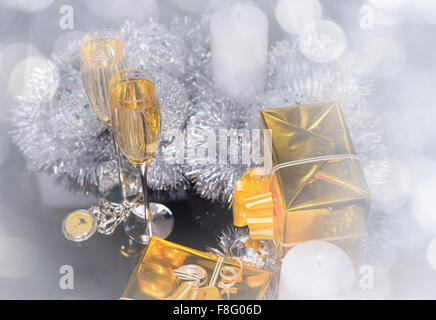 Festa di Natale scintillante Still Life - diffusa vista di orologio da tasca, bicchieri di champagne, regali avvolti in carta oro, candela con la fiamma e decorazioni color argento. Foto Stock